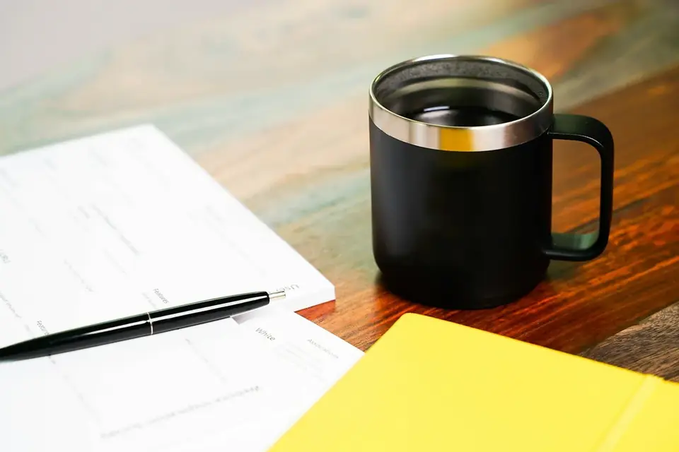 Caneta, bloco amarelo e caneca sobre uma mesa de madeira