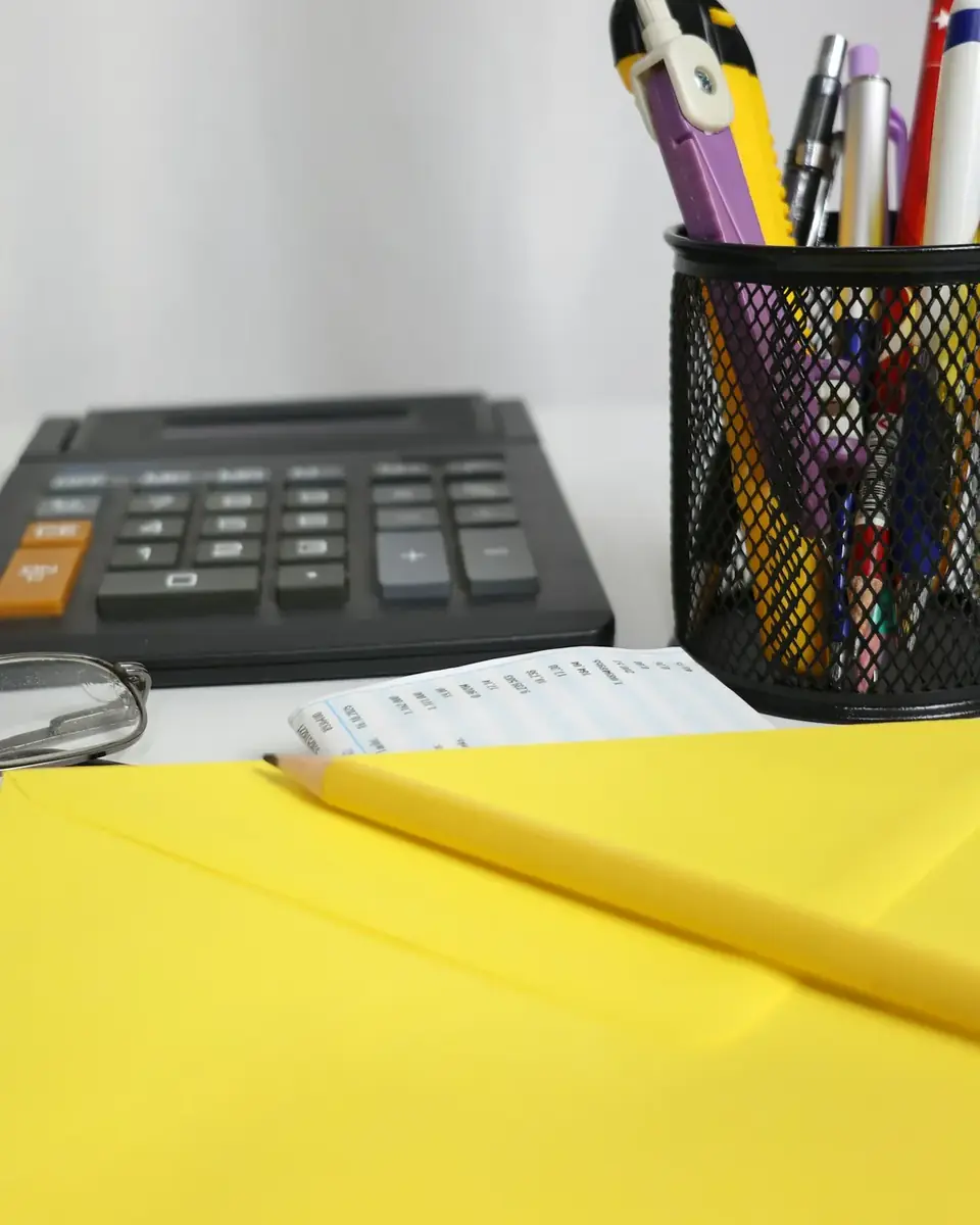 Calculadora, canetas e envelope amarelo sobre a mesa