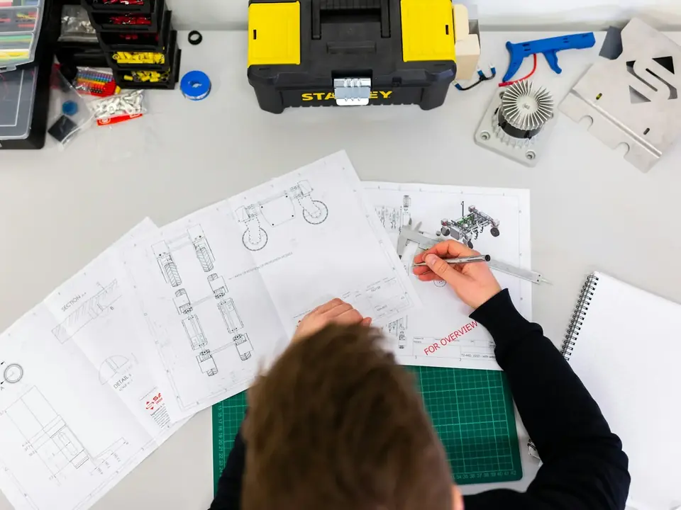 Pessoa medindo desenhos técnicos sobre a mesa, vista de cima